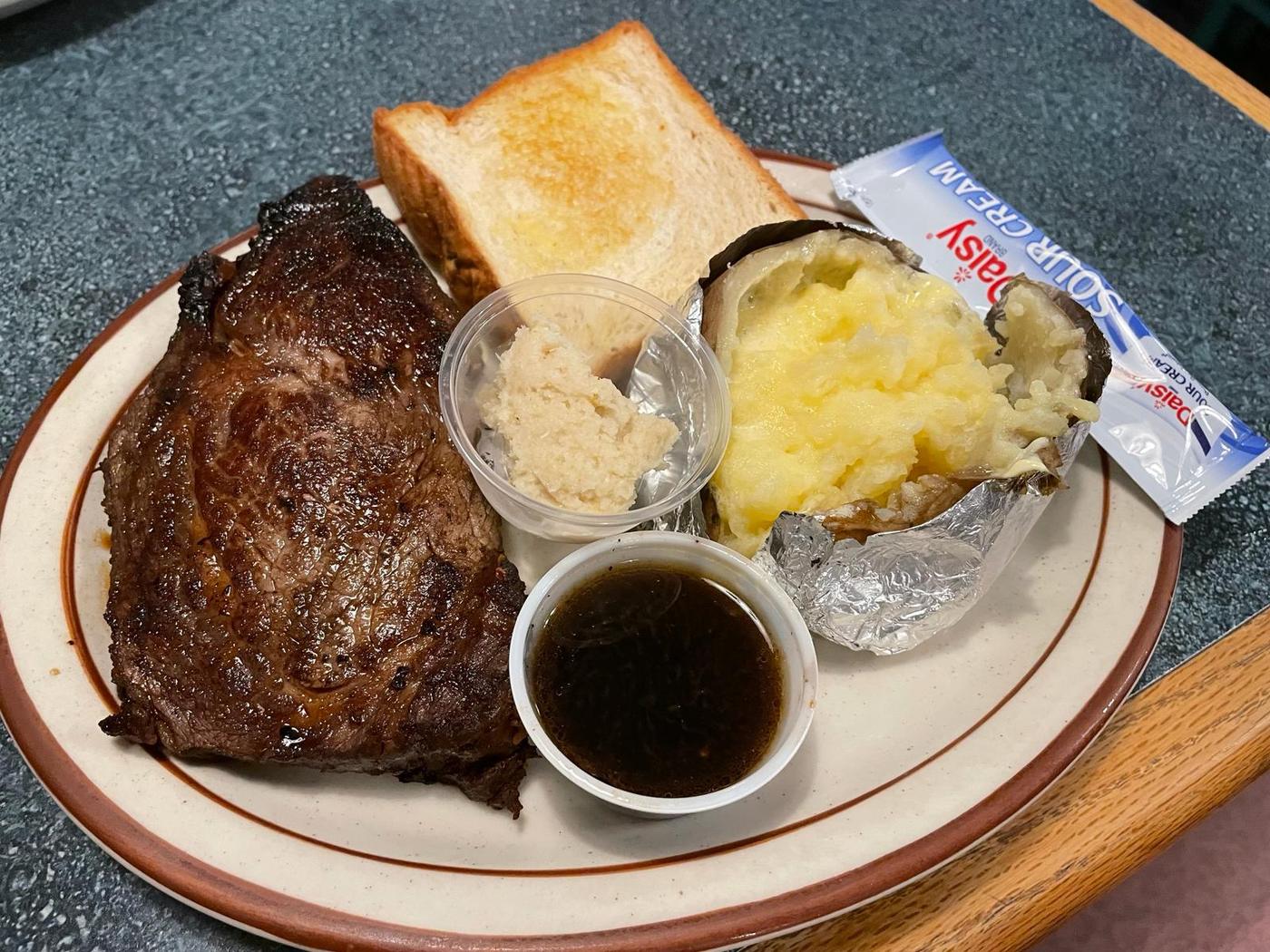A prime rib plate with au jus, horseradish, and a loaded baked potato at Grecian Steak House